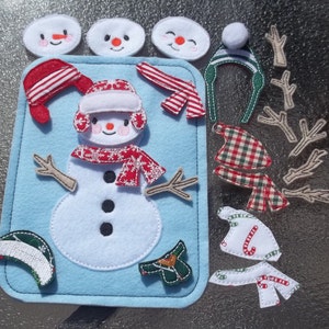 May include: A felt snowman activity set with various accessories. The set includes a light blue felt base with a large white snowman, and several detachable pieces like hats, scarves, and arms. The accessories are red, green, and white.