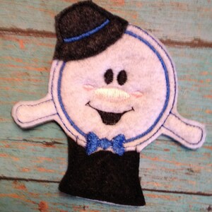 May include: A felt snowman-like figure with a black top hat and bow tie. The figure has a white body with blue trim and a smiling face with rosy cheeks. The bottom portion is a black cylinder shape.