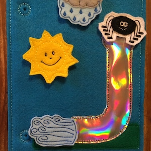 May include: A teal felt weather-themed activity board with a smiling yellow sun, a gray cloud with rain, and a white cloud with wind. A shiny, rainbow-colored tube and a black spider are also attached.