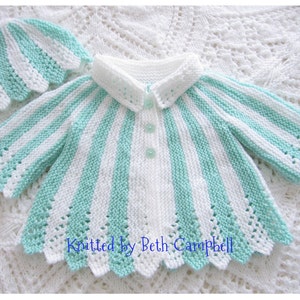 May include: A white and mint green striped knitted baby cardigan with a scalloped edge and a matching hat. The cardigan has a button closure and a white collar.