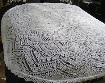 May include: A white crocheted shawl with a delicate lace pattern. The shawl is circular and has a centre point with intricate details.