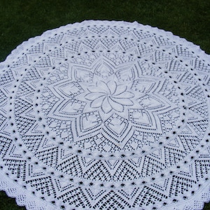 Könnte beinhalten: Eine weiße Häkeltischdecke mit einem zarten floralen Muster in der Mitte.