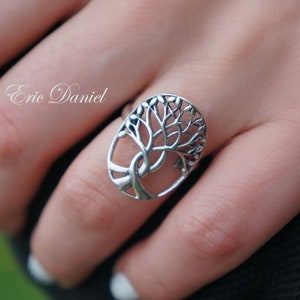 May include: A silver ring with a tree of life design. The ring is on a person's finger.