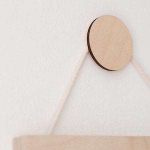 May include: A wooden shelf with a circular wooden hanger attached to a white wall with white string.