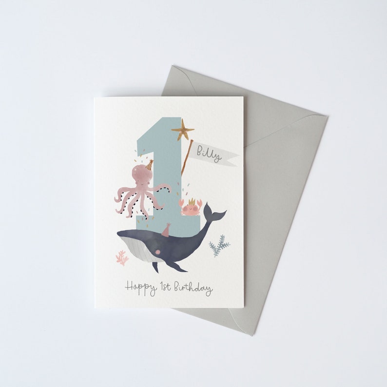 May include: A blue and white birthday card featuring a whale, octopus and crab. The number one is in the background with a gold star and the name "Billy" on a banner. The text "Happy 1st Birthday" is at the bottom of the card.