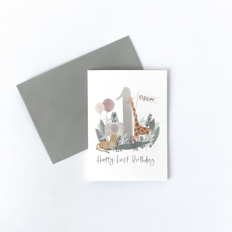 May include: A watercolor illustration of a birthday card with a giraffe, elephant, and lion standing on a number one. The card is white with a gray envelope and says "Happy First Birthday" and "Oscar" on the front.