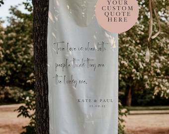 May include: White fabric banner with a quote about true love, "True love is when both people think they are the lucky one." The banner also includes the names "KATE & PAUL" and the date "22.09.25".