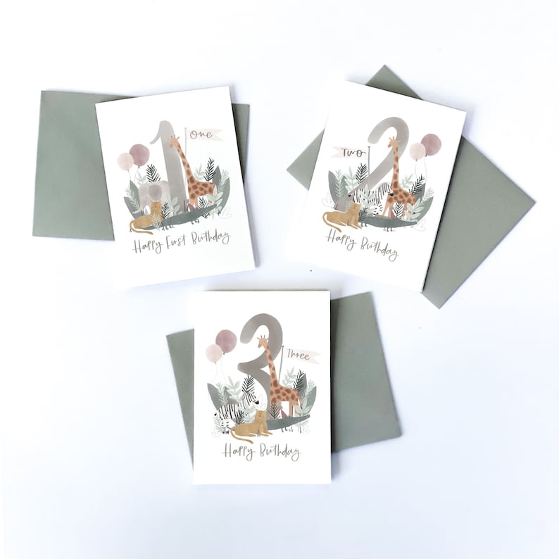 May include: Three cards with a jungle animal theme. Each card features a different number, one, two, and three, with a giraffe and other animals. The cards say "Happy First Birthday", "Happy Birthday", and "Happy Birthday".