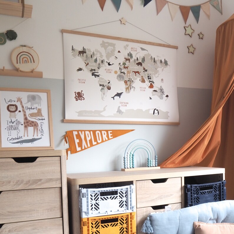 May include: A light wood dresser with two drawers and a white crate on top. A world map with animals and oceans is hanging on the wall above the dresser. A wooden rainbow abacus is on the dresser. The dresser is in a room with a light brown curtain.