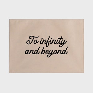 May include: Beige canvas kitchen towel with black text that reads "To infinity and beyond".