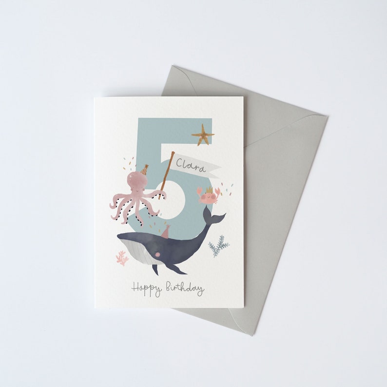 May include: A blue and white birthday card featuring a whale, octopus, and the number 5. The card reads "Happy Birthday" and "Clara" on a banner.