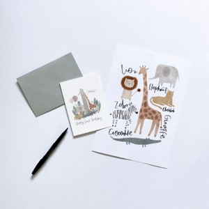 May include: A card with a giraffe, zebra, lion, elephant, cheetah, and crocodile. The card says "Happy First Birthday" and "one".