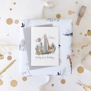 May include: A white card with a watercolor illustration of a giraffe, elephant, lion, and crocodile surrounding the number one. The card says "One" and "Happy First Birthday".