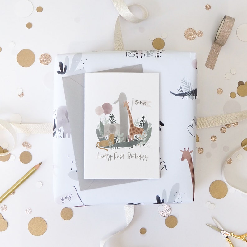 May include: A white card with a watercolor illustration of a giraffe, elephant, lion, and crocodile surrounding the number one. The card says "One" and "Happy First Birthday".