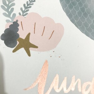May include: A light blue background with a pink and white seashell, a gold starfish, and a grey and white seahorse. The word "Sunday" is written in gold script.