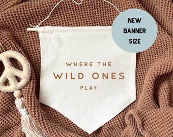 May include: A white canvas banner with the text "Where the Wild Ones Play" hanging on a brown textured wall. The banner is a new size.