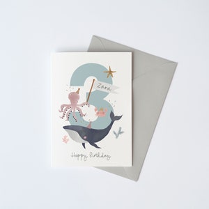 May include: A blue and white birthday card featuring a whale, octopus and crab. The number 3 is in the background with the name Zara on a banner. The text "Happy Birthday" is at the bottom of the card.