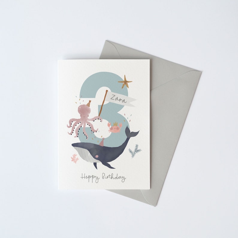 May include: A blue and white birthday card featuring a whale, octopus and crab. The number 3 is in the background with the name Zara on a banner. The text "Happy Birthday" is at the bottom of the card.
