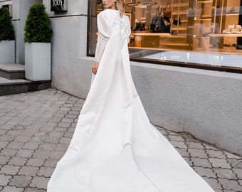 Puede incluir: Una mujer con un vestido blanco y una larga cola camina de espaldas a la cámara frente a una tienda con un letrero que dice "TODS".