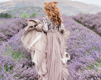 May include: A woman in a long, flowing, light purple dress with floral embroidery walks through a field of lavender.