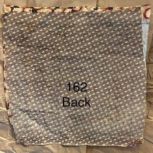 May include: A folded piece of fabric with a brown background and a repeating white dot pattern. The text "162 Back" is printed in black. The edges have a patterned border with red and black accents.