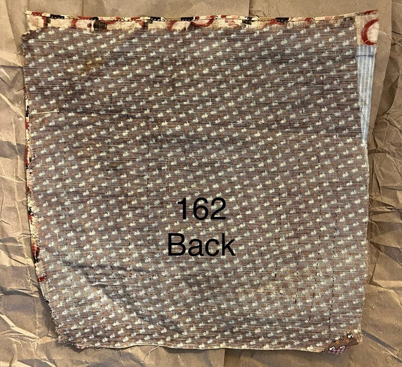 May include: A folded piece of fabric with a brown background and a repeating white dot pattern. The text "162 Back" is printed in black. The edges have a patterned border with red and black accents.