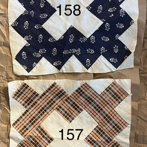 May include: Two vintage quilt blocks. One block features a navy blue floral pattern with the number "158" in the center. The other block has a plaid pattern in shades of orange, black, and white, with the number "157".