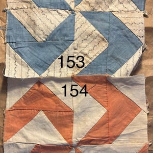 May include: Two antique quilt blocks. The top block features blue and cream fabric with a geometric design. The bottom block has an orange and cream geometric pattern. Each block has a number printed on it: 153 and 154.