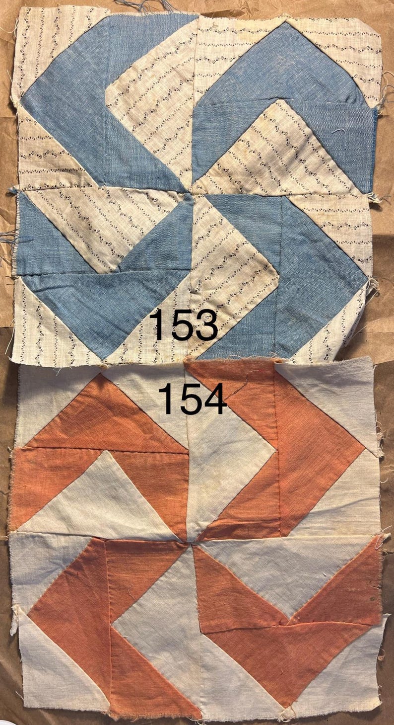 May include: Two antique quilt blocks. The top block features blue and cream fabric with a geometric design. The bottom block has an orange and cream geometric pattern. Each block has a number printed on it: 153 and 154.