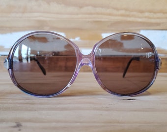 May include: A pair of round, oversized sunglasses with a purple frame and brown lenses.