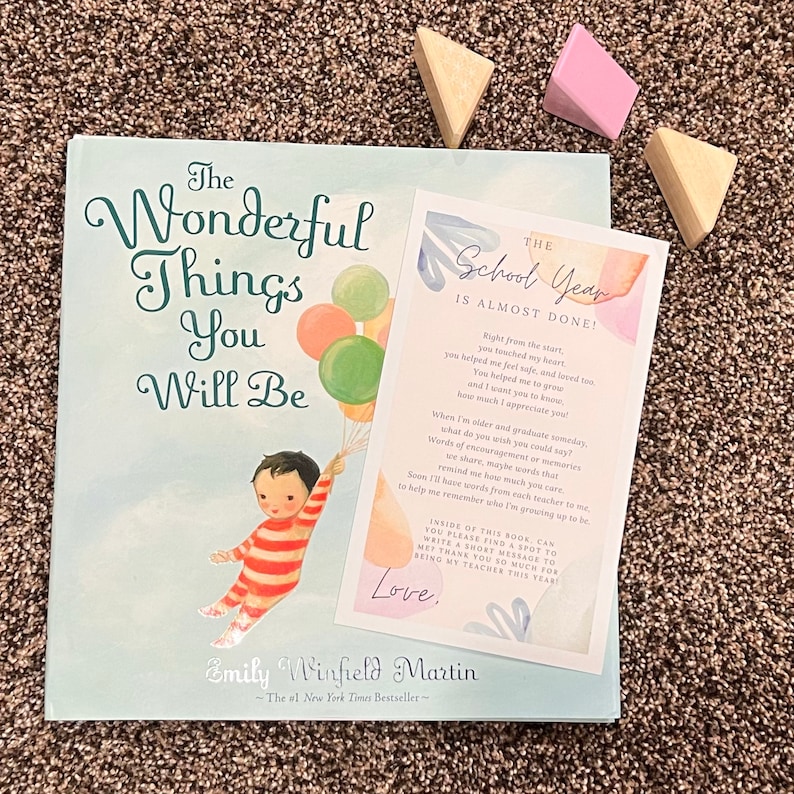 May include: A pink and blue card with the text "The School Year is Almost Done!"  The card has a watercolor background and features a message about the end of the school year. The card is sitting on top of a book titled "The Wonderful Things You Will Be" by Emily Winfield Martin.