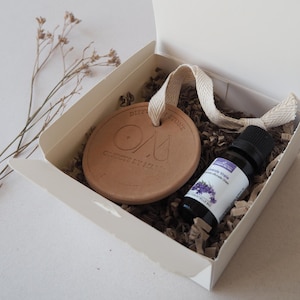Könnte beinhalten: Geschenkset in einer weißen Box mit einem Terrakotta-Diffusorstein mit dem Text "DIFFUSION STONE" und "OBJECTIF BY IZANA", einer kleinen Flasche ätherischem Lavendelöl und dekorativem Füllmaterial.