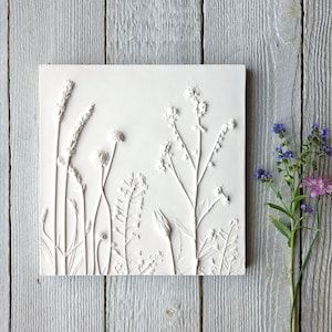 Può includere: Arte da parete in gesso bianco con un design a rilievo di vari fiori selvatici ed erbe. I fiori sono disposti in una fila verticale e sono tutti in tonalità di bianco.