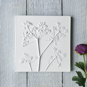 Może przedstawiać: Biała kwadratowa dekoracja ścienna z wypukłym wzorem delikatnego kwiatu w minimalistycznym stylu.