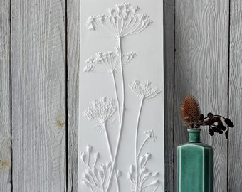 May include: White rectangular wall art with a raised 3D design of a cluster of white flowers with stems. The flowers are arranged in a vertical pattern.