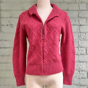 Peut inclure: Un cardigan rose vif à fermeture éclair avec un motif en tricot ajouré texturé. Le cardigan présente un col, des manches longues et des bordures côtelées. La fermeture éclair s'étend sur toute la longueur.