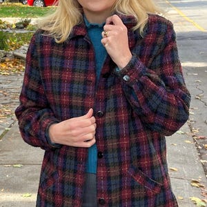 Könnte beinhalten: Eine langärmelige, karierte Jacke in einem blau-rot-schwarzen Farbmuster. Die Jacke hat einen Knopfverschluss und eine Tasche auf der linken Seite.