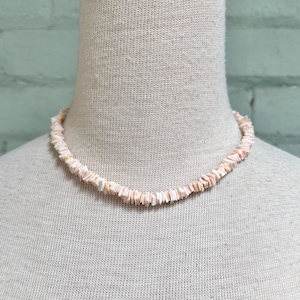 以下が含まれることがあります： 小さな平らな貝殻のピースで作られたピンクの貝殻のネックレス。ネックレスは白いマネキンにあります。