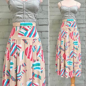 May include: A two-piece outfit comprising a grey denim-style top and a high-waisted skirt. The skirt is beige with a colourful pattern of red, blue, and white abstract shapes. The top has a sweetheart neckline and a fitted bodice.