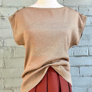 Puede incluir: Una blusa de punto metálica marrón con mangas cortas y cuello redondo. La blusa tiene un sutil patrón de rayas horizontales.