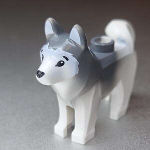 Könnte beinhalten: Eine Husky-Hundefigur aus Kunststoff in Grau- und Weißtönen. Der Spielzeughund hat eine schwarze Nase und Augen mit einem weißen Fleck im Gesicht. Der Hund hat ein zylindrisches Loch auf dem Rücken.