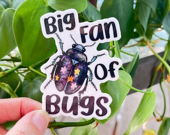 May include: A die-cut sticker featuring a beetle with a dark, galaxy-patterned shell decorated with small yellow and pink stars. The text "Big Fan Of Bugs" is printed in bold, black, rounded letters surrounding the central insect illustration.