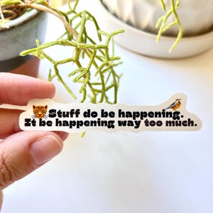 May include: White sticker with a black and white cartoon leopard face, a yellow bird, and the text "Stuff do be happening. It be happening way too much."