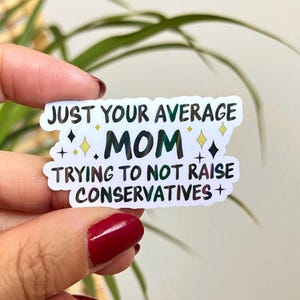 May include: White sticker with black text that reads "Just your average mom trying to not raise conservatives". The text is surrounded by small black and yellow stars.