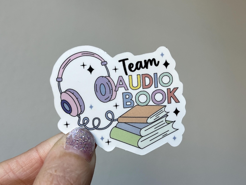 May include: A white sticker with a pink and purple headphone, a stack of books, and the text "Team Audio Book" in rainbow colors.