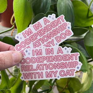 May include: Two pink and white stickers with the text "I'm in a codependent relationship with my dog" and "I'm in a codependent relationship with my cat".