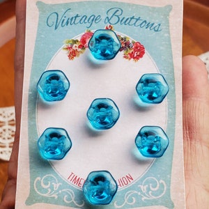 May include: Seven hexagonal, transparent, turquoise vintage buttons are displayed on a card with the words "Vintage Buttons". The card has a floral design and the words "TIME FASHION". The buttons are made of a clear, shiny material.