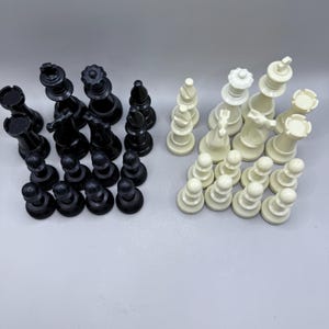 May include: A complete chess set with black and white pieces. The black pieces include rooks, knights, bishops, a queen, a king, and pawns. The white pieces mirror the black pieces. The chess pieces are arranged on a light gray surface.