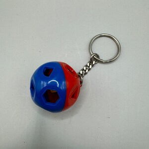 May include: A red and blue plastic ball with geometric cutouts attached to a silver key chain.