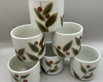 May include: Set of six white ceramic teacups with a brown and green floral design. The cups are stacked in a pyramid shape.